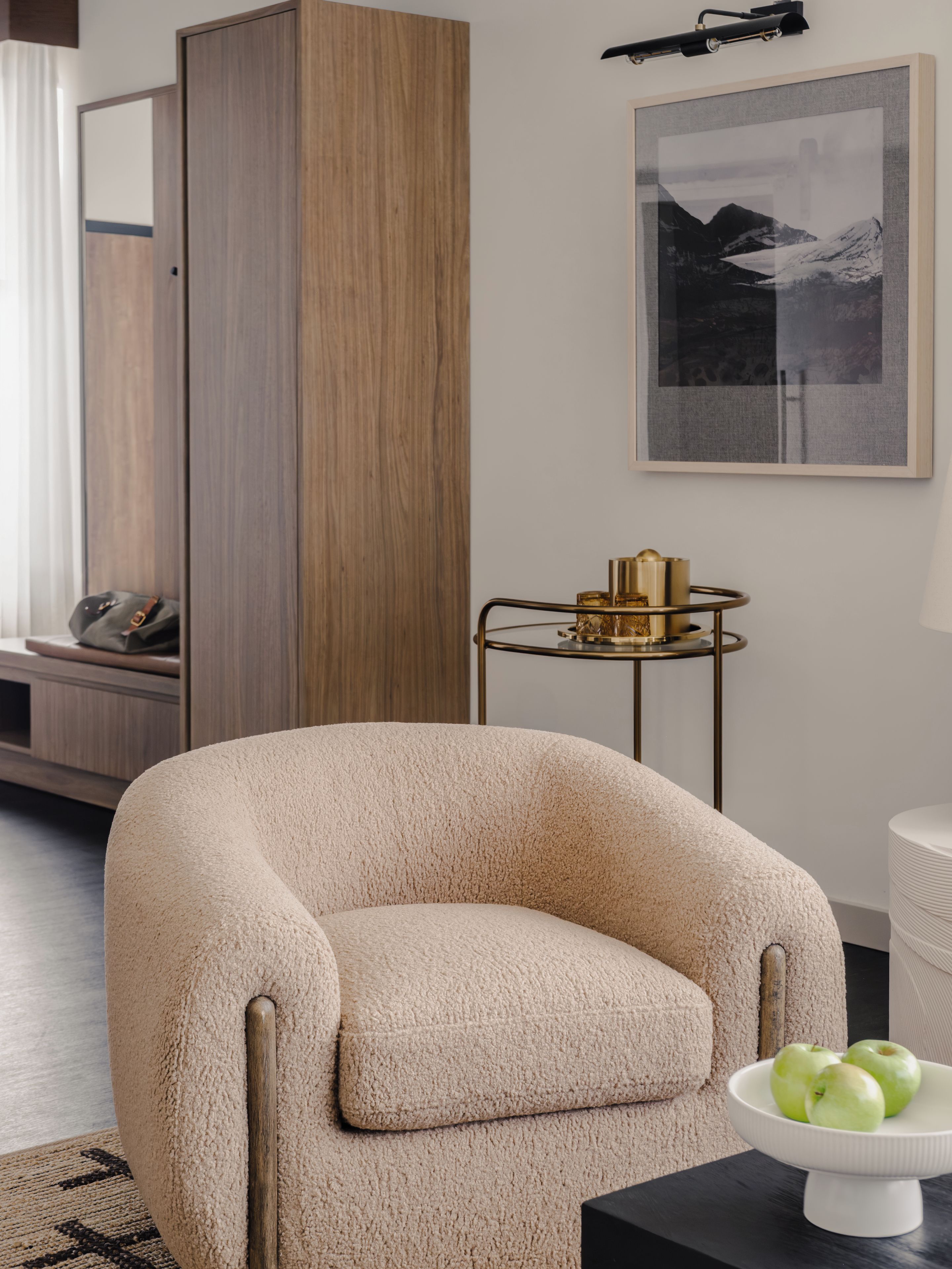Una habitación con un sillón grande y mullido, una mesita auxiliar con objetos decorativos y un cuadro de paisaje en la pared.