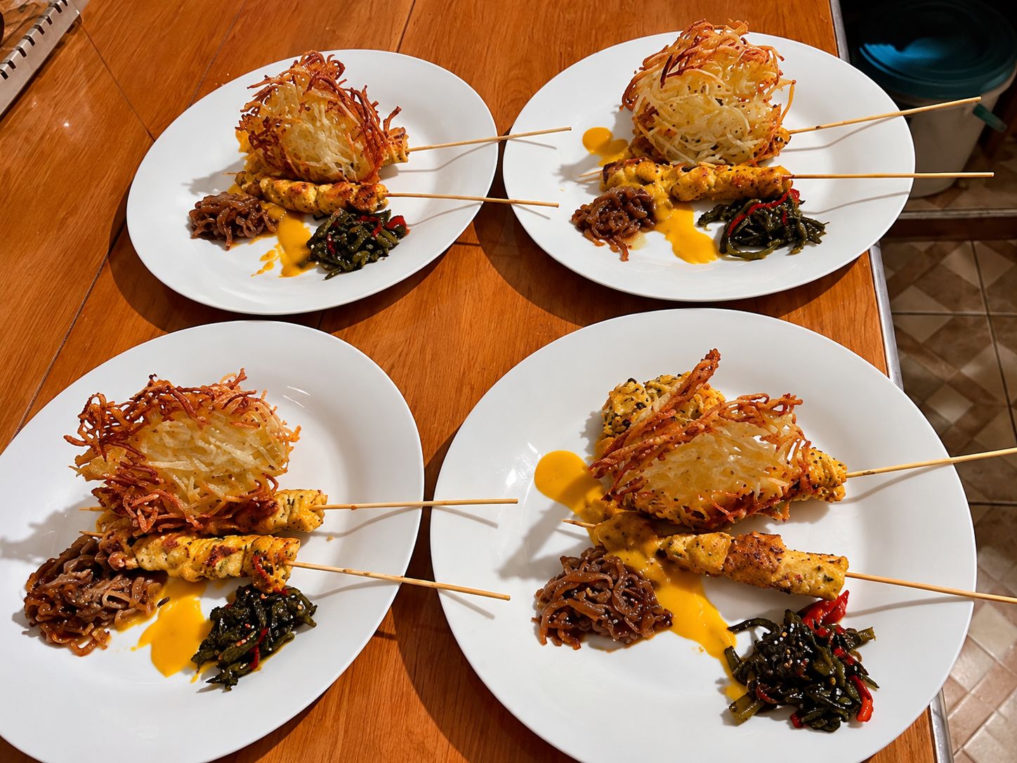 Vier borden met eten, spiesjes, gefrituurde gerechten en groenten op een houten tafel.