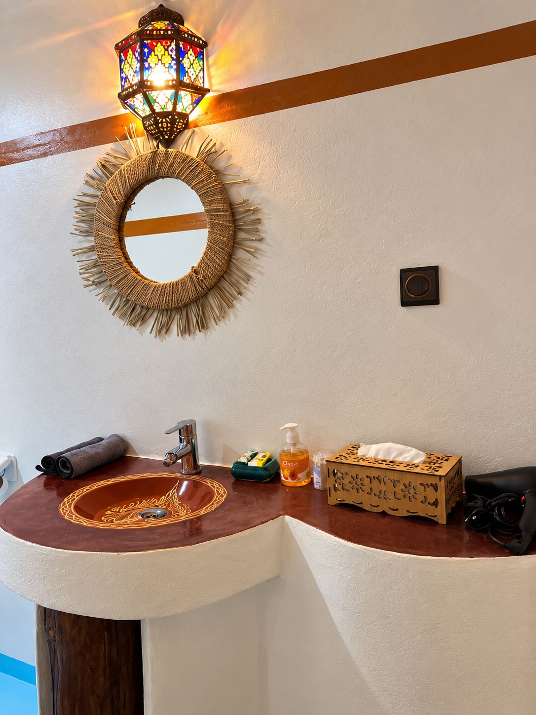 Ein Badezimmer mit einem runden Spiegel, einer Holzleiste an der Wand, einem Waschbecken mit dekorativer Schale und einer wandmontierten Lampe.