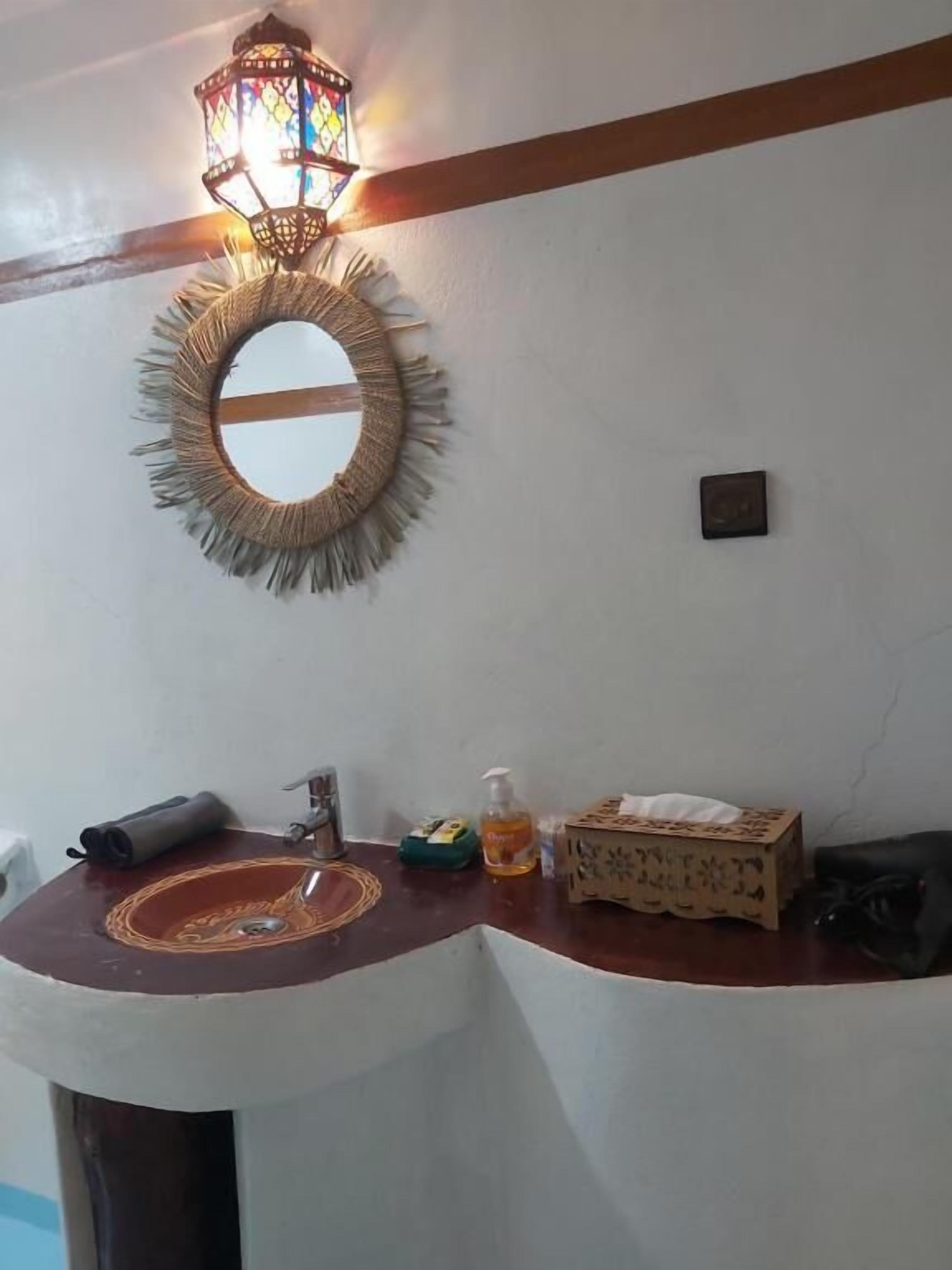 A bathroom with a round mirror, a sink, a hanging light fixture, and toiletries on the counter.