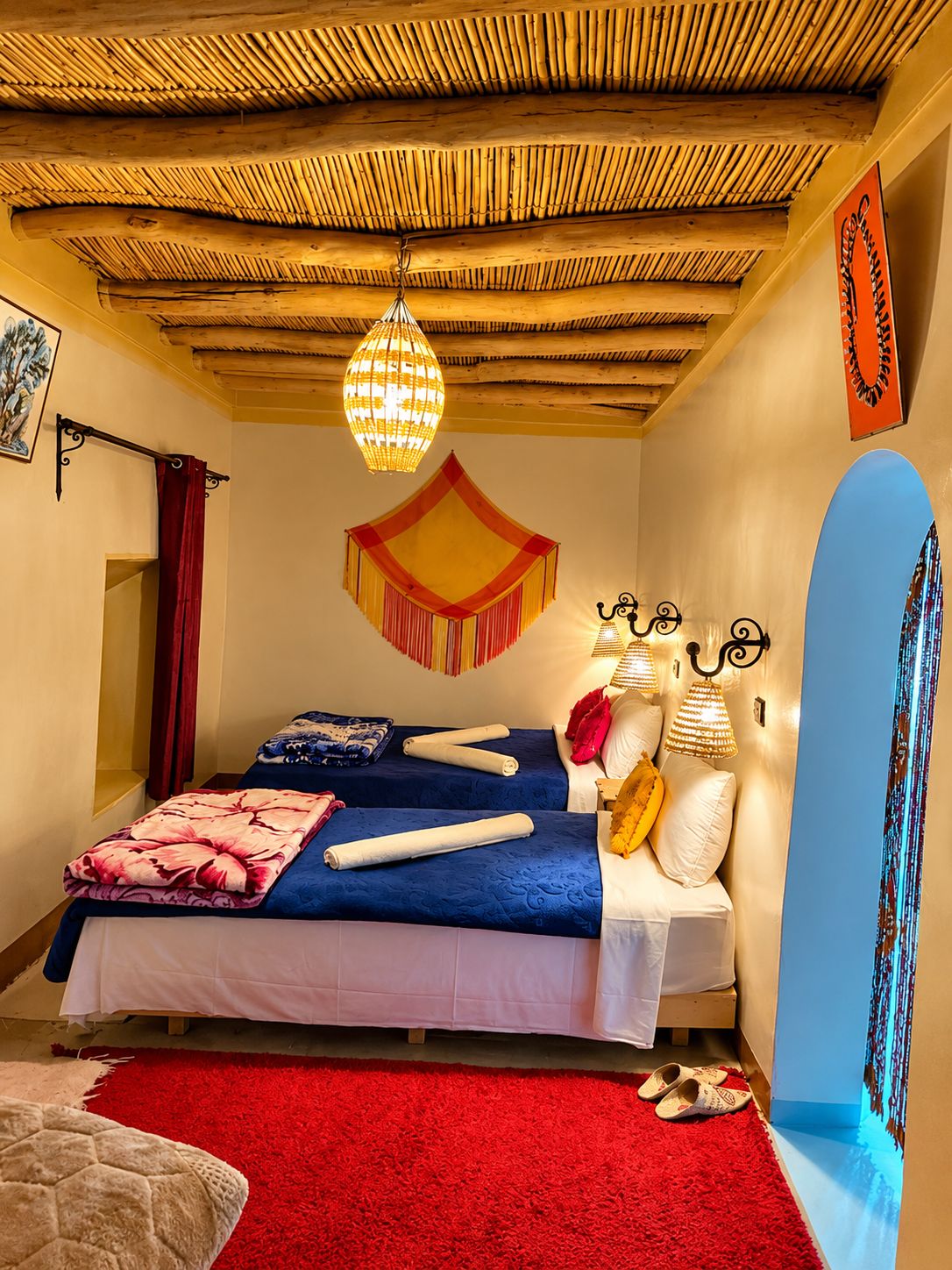 Una habitación con cama, alfombra roja, lámpara colgante y lámpara de pared.