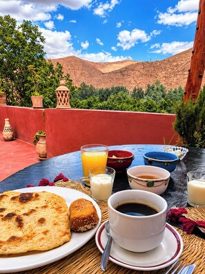 A table set with a meal, including flatbread, a cup of coffee, and bowls of food, with a mountainous landscape in the background.