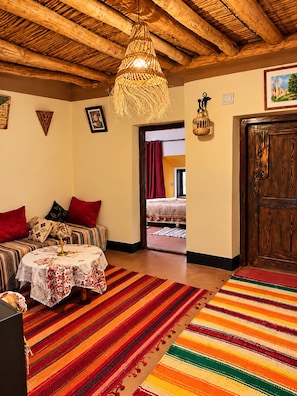 Una habitación acogedora con techo de madera, una cama con cortinas rojas, una mesa con mantel estampado y una alfombra a rayas colorida.