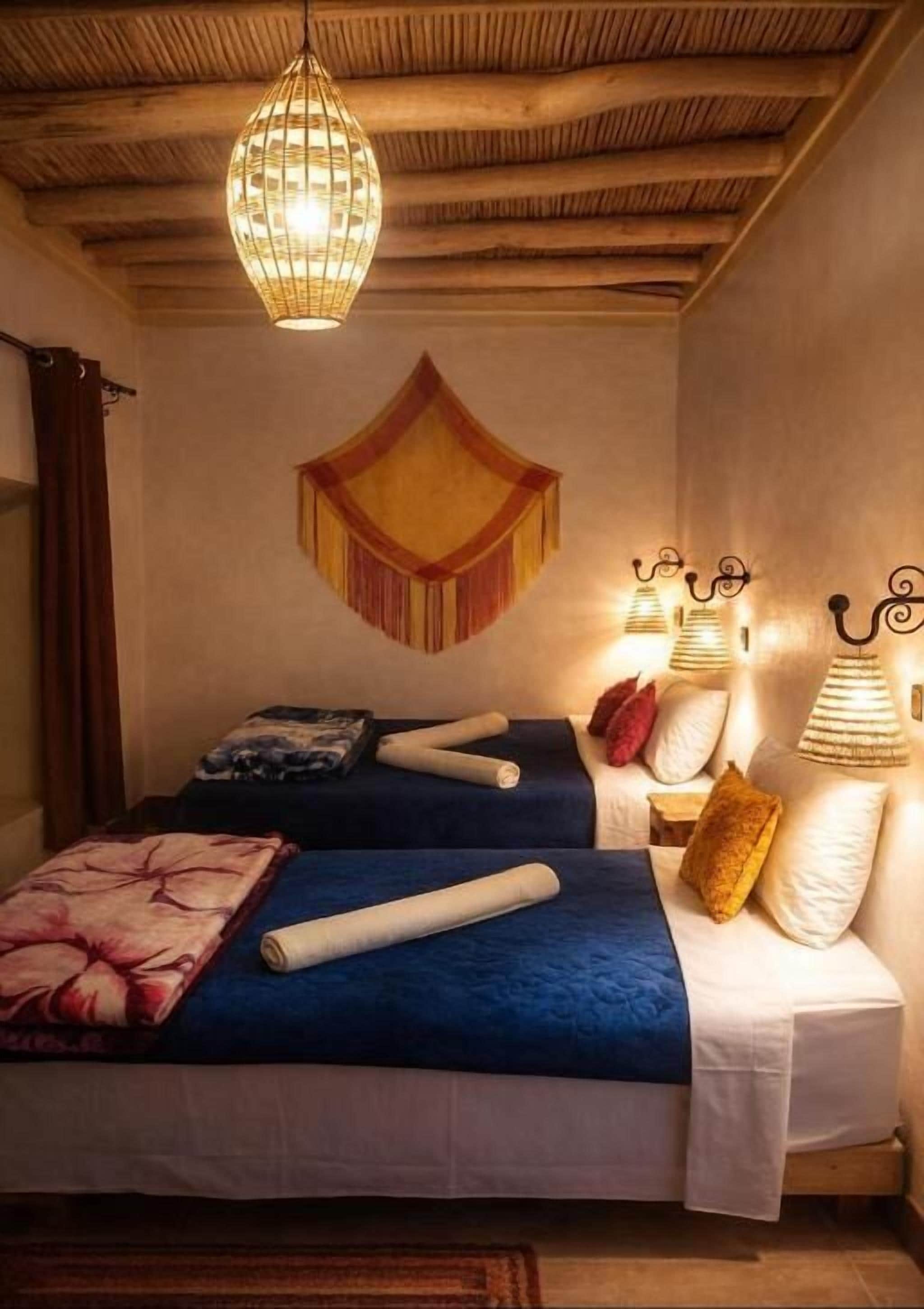 A room with two beds, a hanging light fixture, and a wall hanging.
