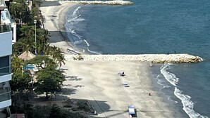 Vista costeira com uma praia, um penhasco rochoso e um edifício com varandas viradas para o mar.
