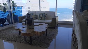 Uma sala de estar com um sofá, uma mesa de centro e vista para o mar.