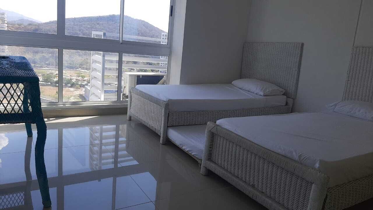 A hotel room with two beds, a chair, and a large window with a view of buildings and hills.