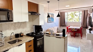 Eine moderne Küche mit Mikrowelle, Herd und Spüle, ein Essbereich mit Tisch und Stühlen sowie ein Fenster mit Vorhängen.