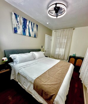 Ein Hotelzimmer mit Bett, Deckenventilator, einem Bild an der Wand und einem Fenster mit Vorhängen.