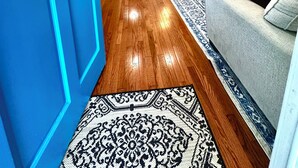 Una sala de estar con puerta azul, piso de madera, sofá gris, una mesa de centro, un televisor de pantalla plana montado en la pared y un tapete estampado.