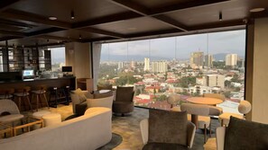 Een moderne lounge met een bar, comfortabele zitplaatsen en een groot raam met uitzicht over de stad.