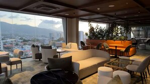 Un espace de détente moderne comprenant un canapé, des fauteuils, une table basse et une vue sur le paysage urbain.
