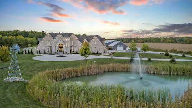 A large stone house with a pond, a windmill, and a barn.