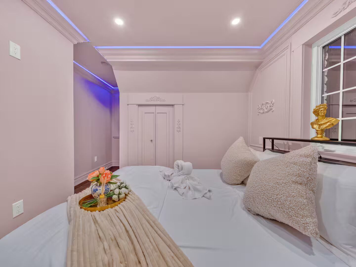 A bedroom with a bed, pillows, a decorative vase, and a bust on a nightstand.