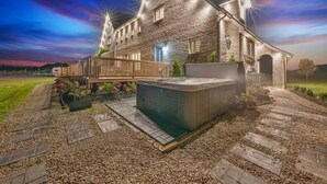A large stone house with a hot tub, a wooden deck, and a well-maintained garden.