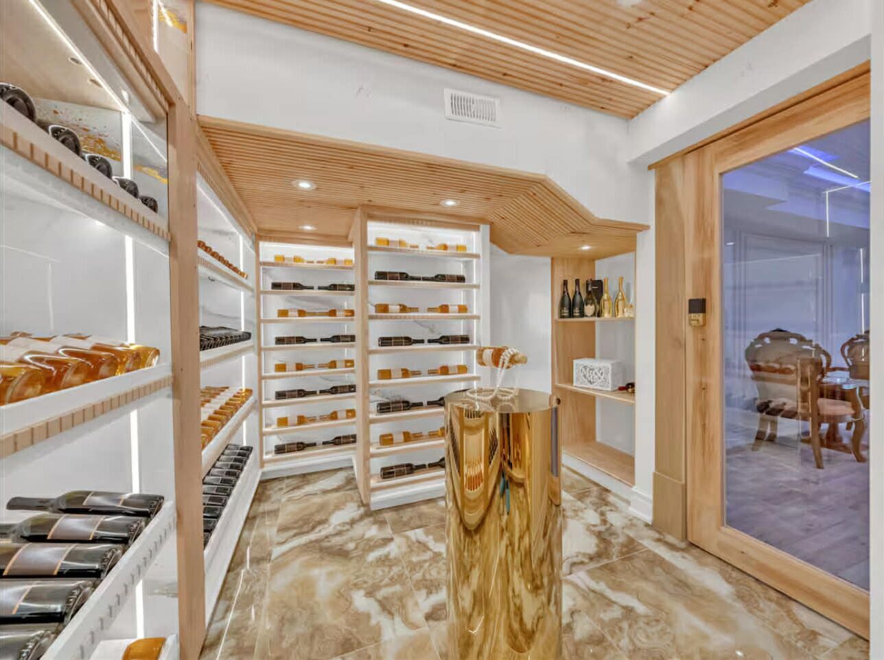 A wine cellar with shelves of bottles, a wooden counter, and a glass door leading to a dining area.