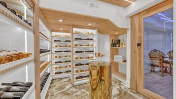 A wine cellar with shelves of bottles, a wooden counter, and a glass door leading to a dining area.