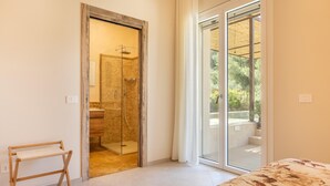 Une chambre avec un lit, un bureau en bois, une douche en verre et une porte-fenêtre coulissante donnant sur un espace extérieur.