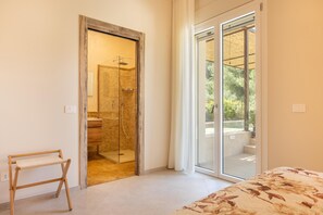 A bedroom with a bed, a wooden desk, a glass shower, and a sliding glass door leading to an outdoor area. - Villa Essenza Di Pace - Nardò (Nardò)