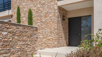 A modern building with a stone facade, a dark door, and a small garden with plants and flowers.
