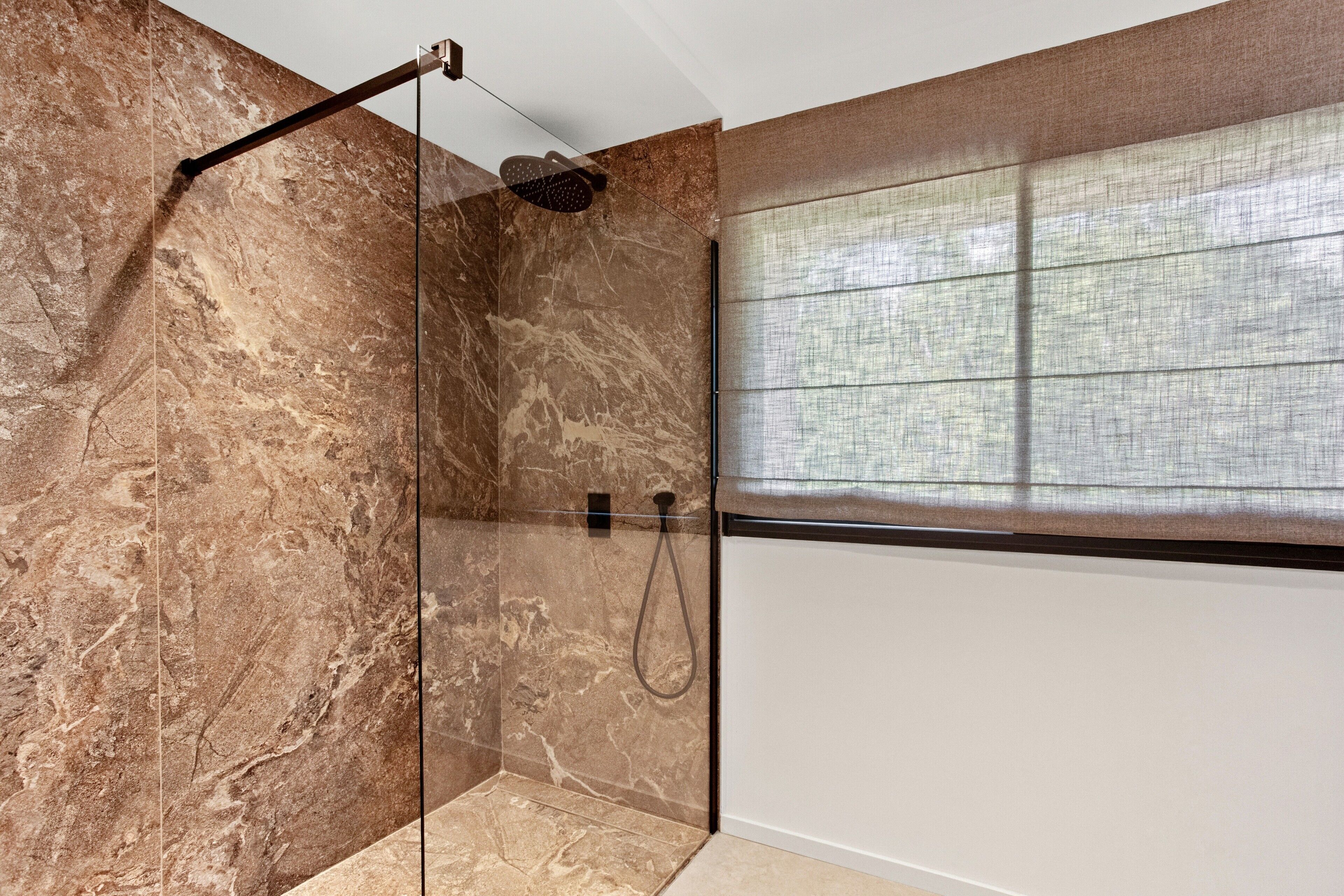 A modern bathroom with a glass-enclosed shower, marble walls, and a window with a view.