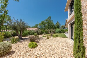 A landscaped garden with a variety of trees and shrubs, a gravel pathway, and a building with a stone facade.