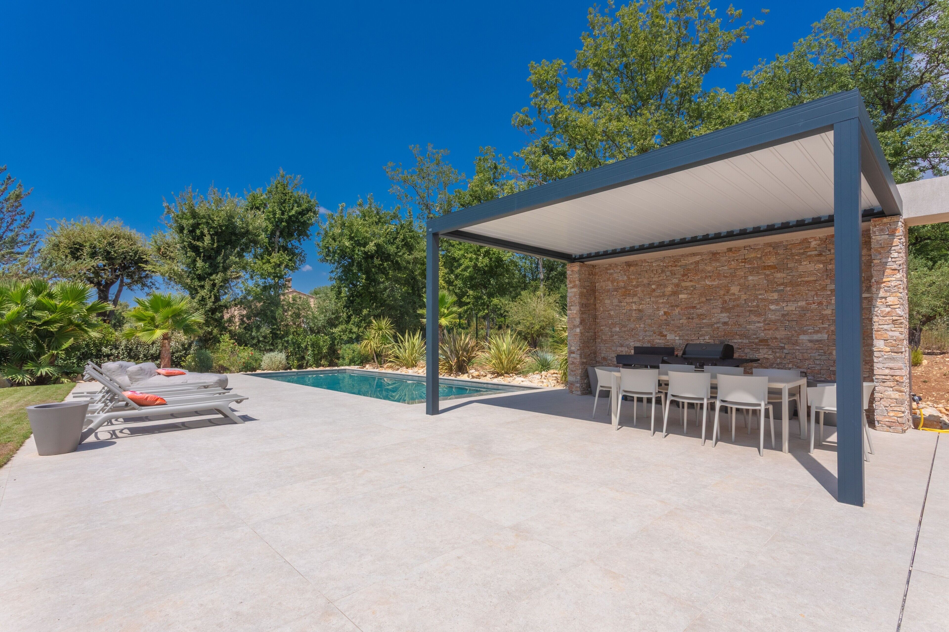 Un patio al aire libre con piscina, sillones de descanso y zona de barbacoa.