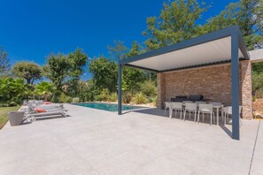 An outdoor patio with a pool, lounge chairs, and a barbecue area.