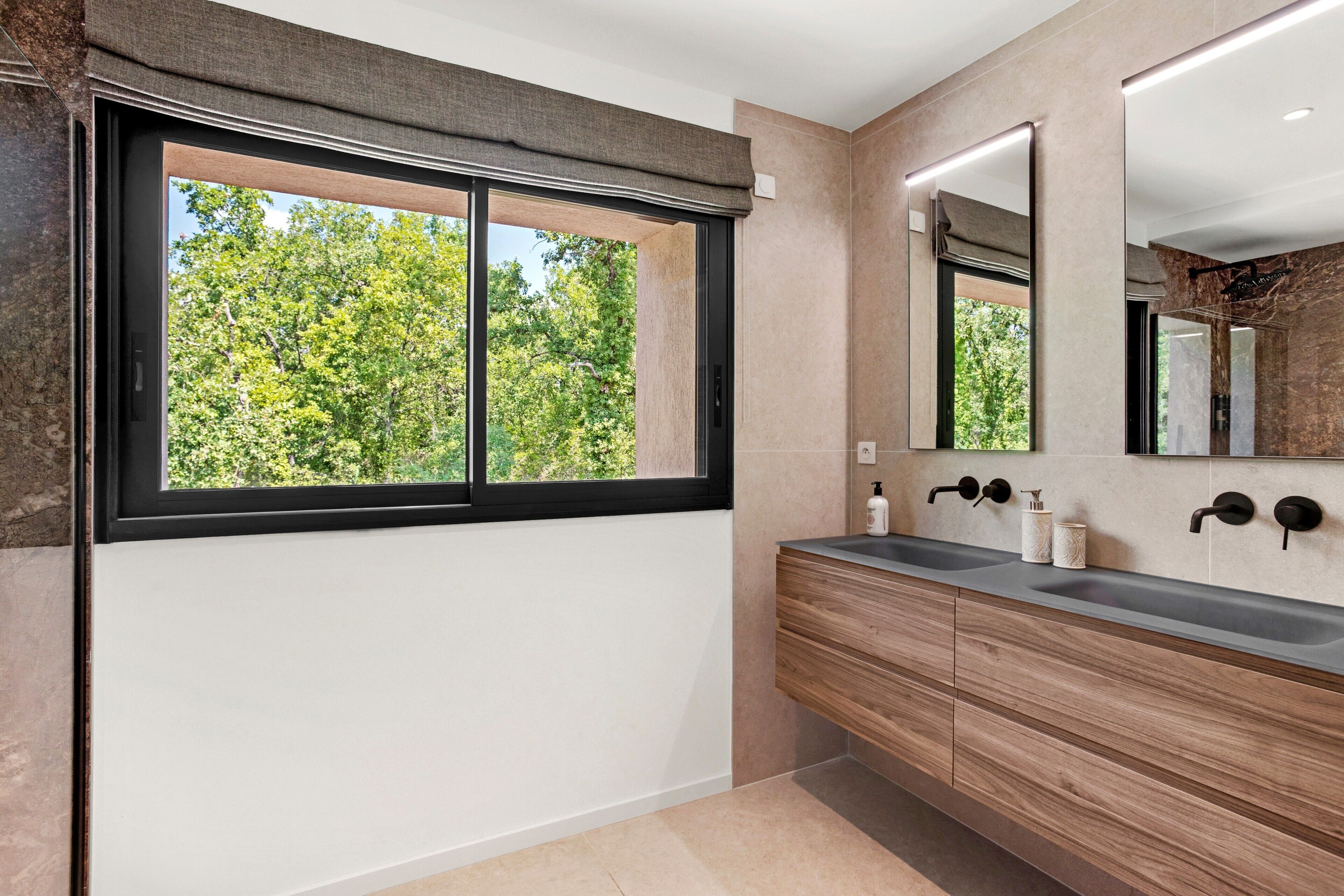 A bathroom with a large window, a mirror, and a wooden vanity.