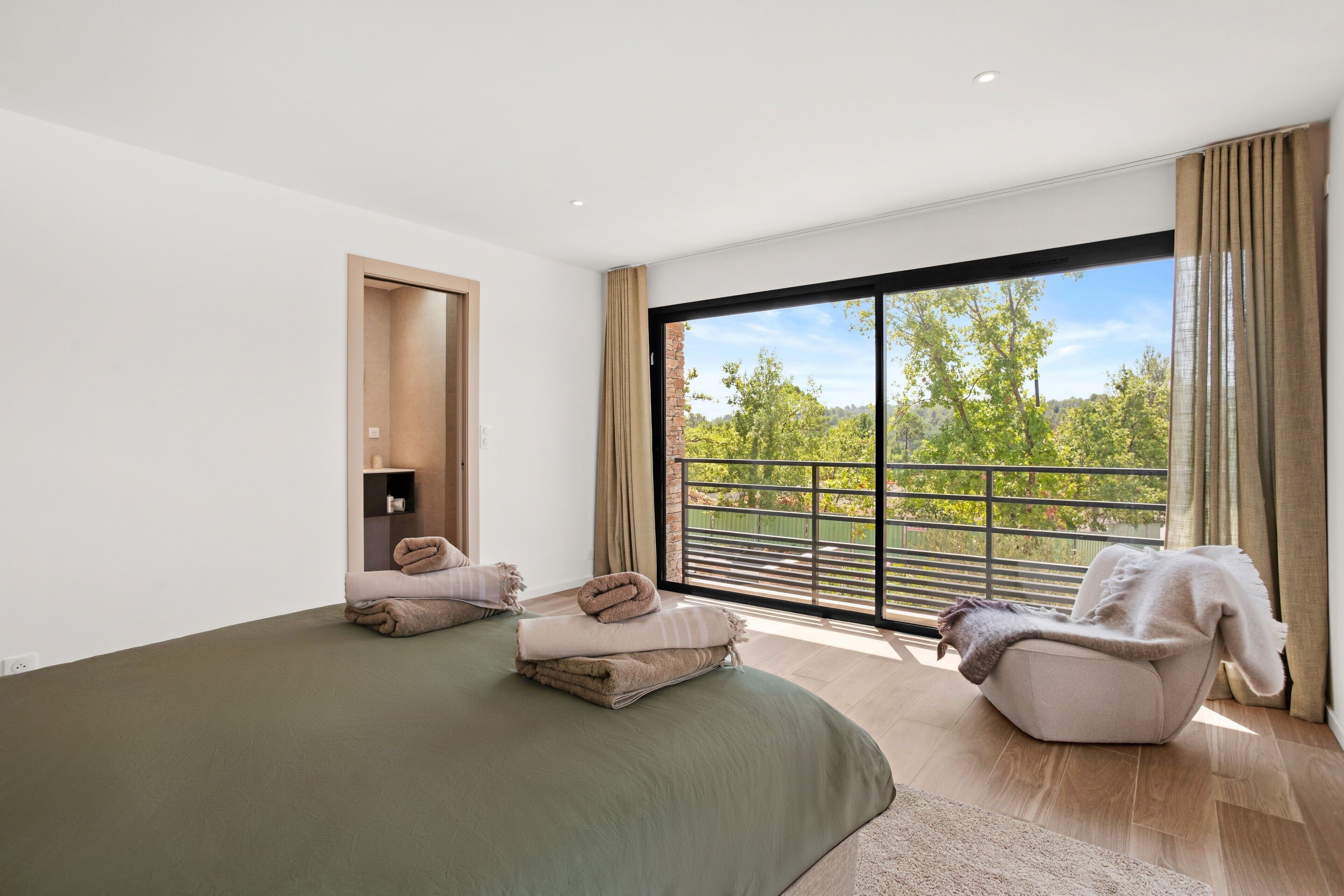 Une chambre moderne avec une grande fenêtre, un lit, une chaise et une petite salle de bain.