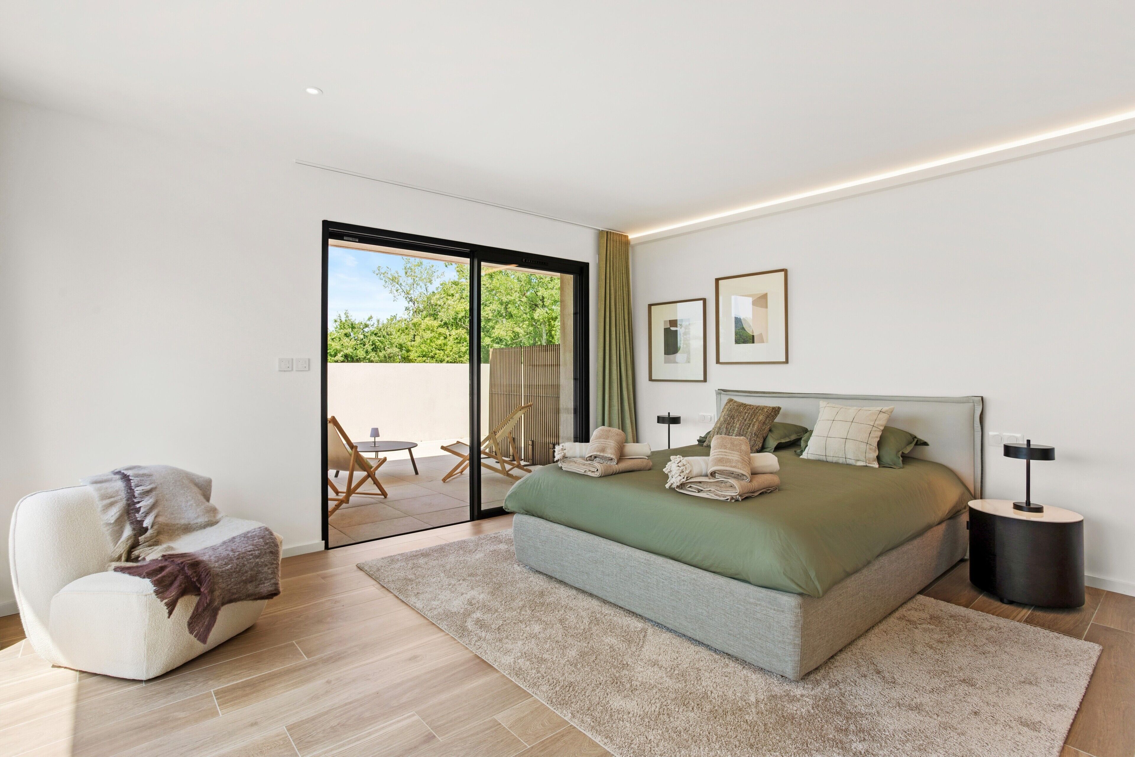 Een moderne slaapkamer met een groot bed, een zithoek en uitzicht door een glazen deur.