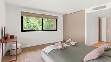 Een slaapkamer met een groot raam, een bed met kussens, een nachtkastje met een lamp, en een spiegel.