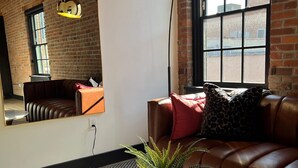 A room with a leather sofa, a round table with a potted plant, a large window with a view, and a brick wall. - Brick & Bed - Riverfront Loft - 405 (St. Louis)