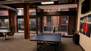 A ping pong table in a room with brick walls, large windows, and a view of the street. - Brick & Bed - Riverfront Loft - 405 (St. Louis)