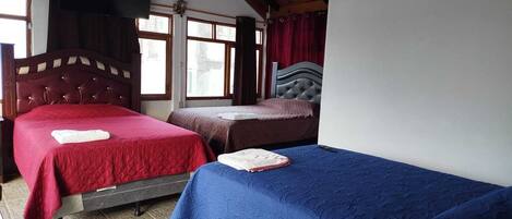 A room with two beds, a wooden ceiling, and large windows.