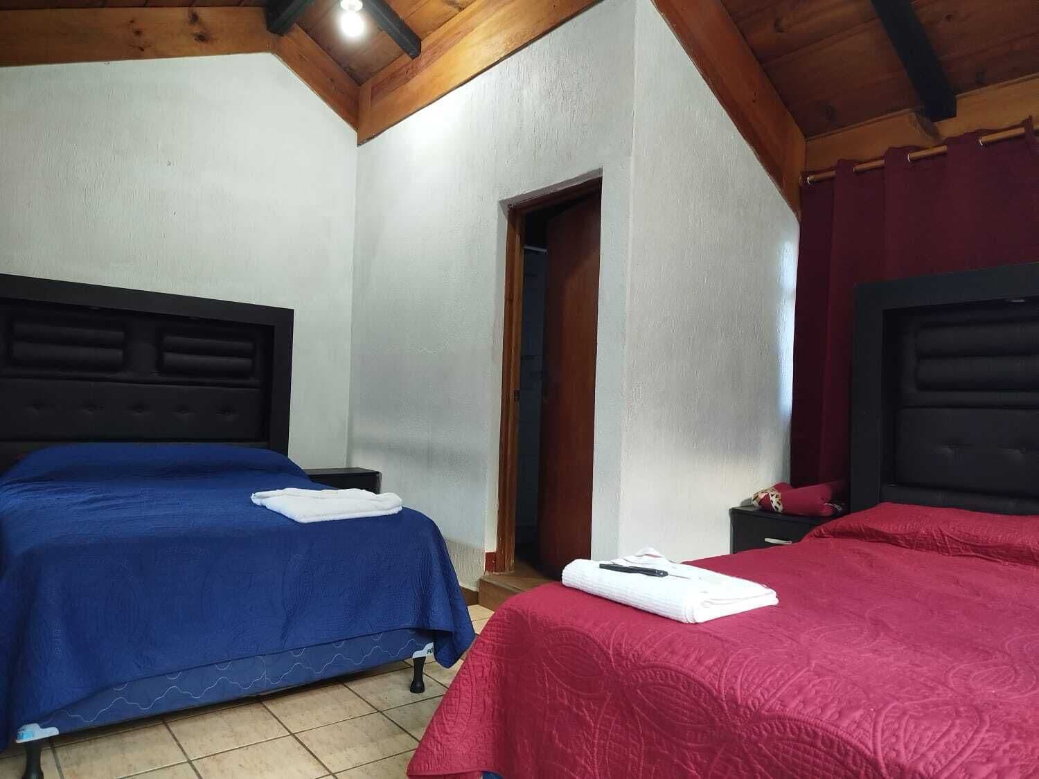 A room with two beds, a wooden ceiling, and a door leading to another room.