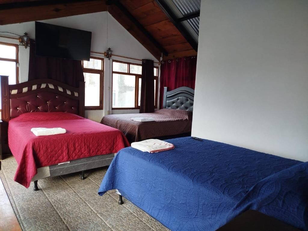 A room with two beds, wooden beams on the ceiling, and a window with curtains.