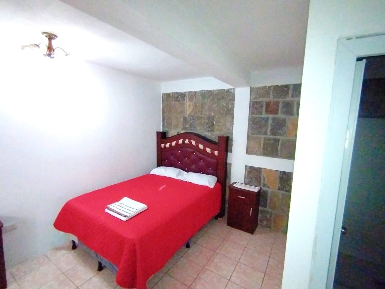 Een slaapkamer met een bed, een nachtkastje, een rode sprei en een stenen muur.