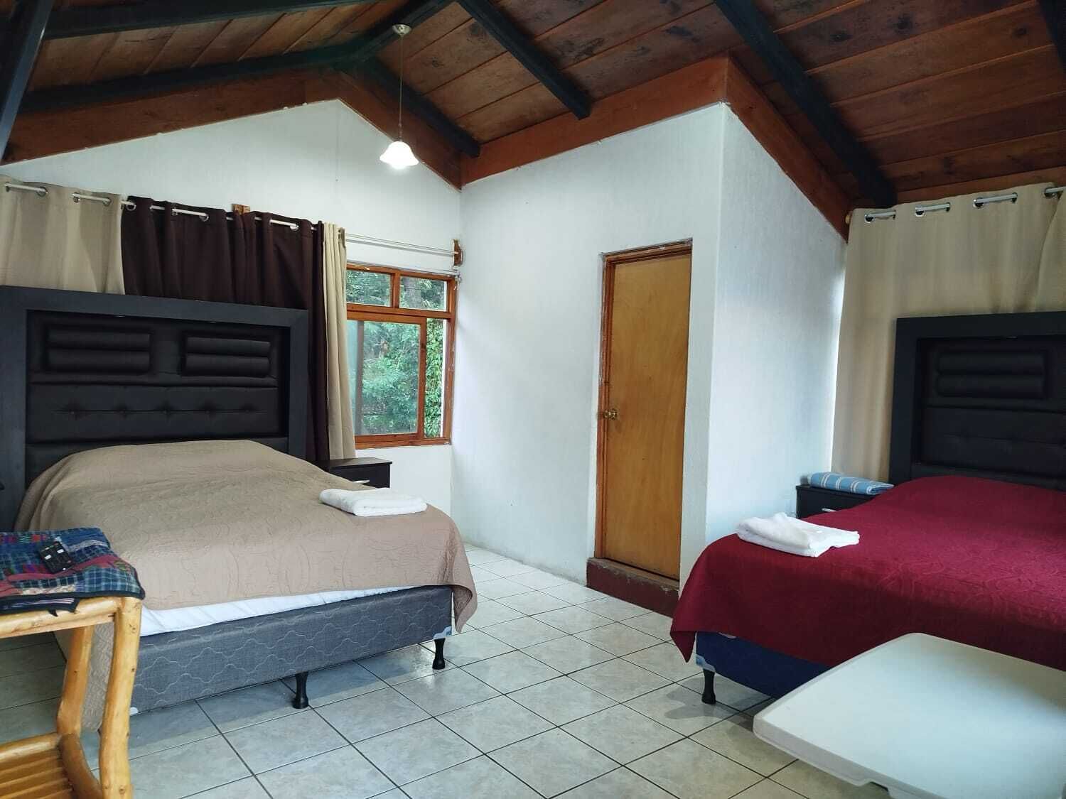 A room with two beds, a wooden ceiling, a window, and a door.