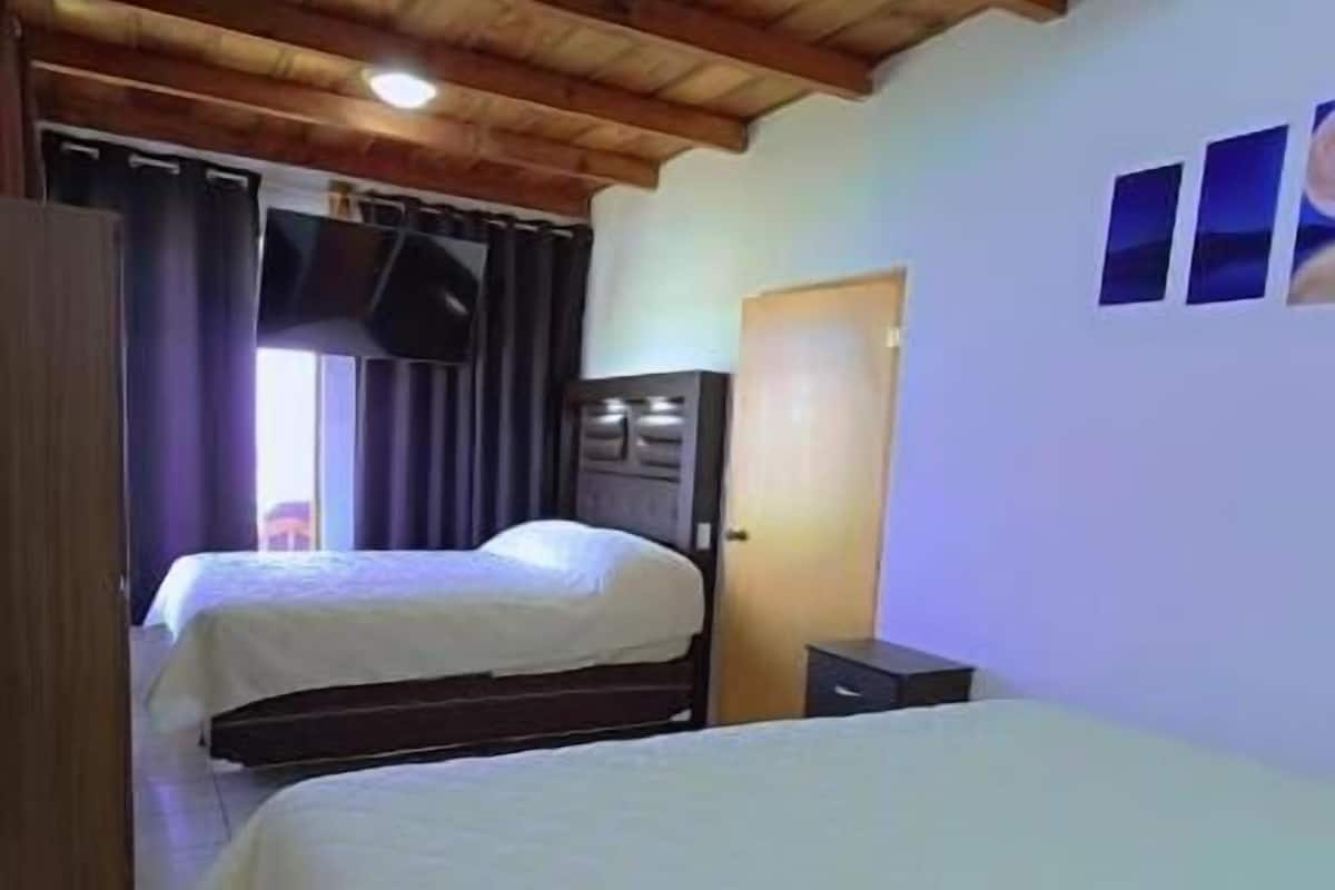 Un dormitorio con dos camas, vigas de madera en el techo, suelo de baldosas y una puerta.