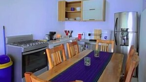 Un tavolo da pranzo in legno con sedie, un angolo cottura con pensili ed elettrodomestici, e un pavimento piastrellato.