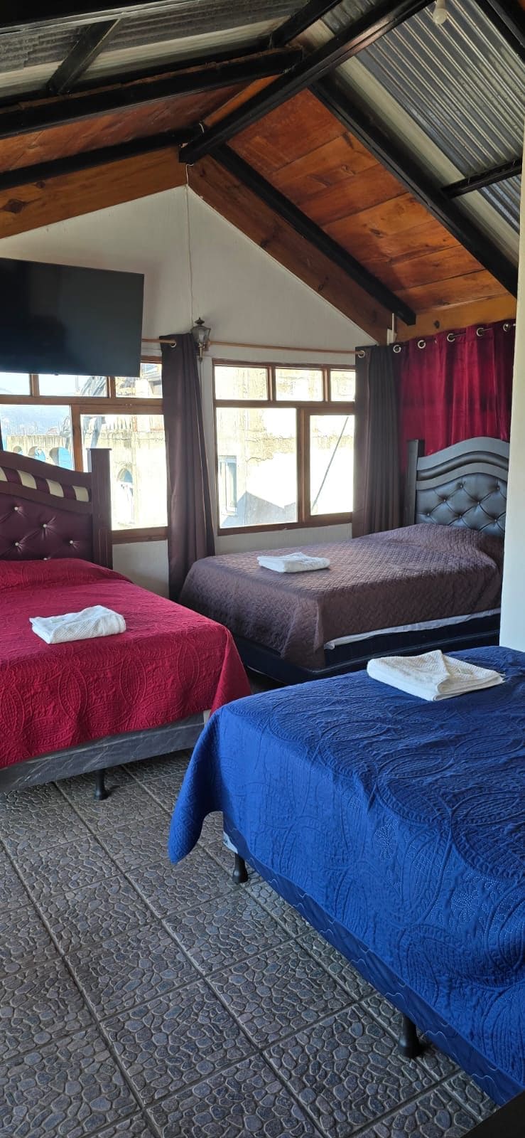 A room with two beds, a wooden ceiling, and a window with curtains.