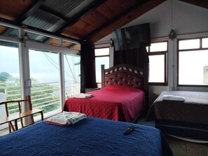 A bedroom with a large window, a bed with a red bedspread, and a second bed with a blue bedspread. - Hotel Victoria Atitlan (San Pedro La Laguna)