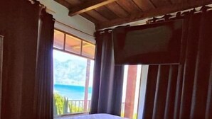 Camera da letto con soffitto in legno, un letto con biancheria bianca, una finestra con tende e vista sull'esterno.