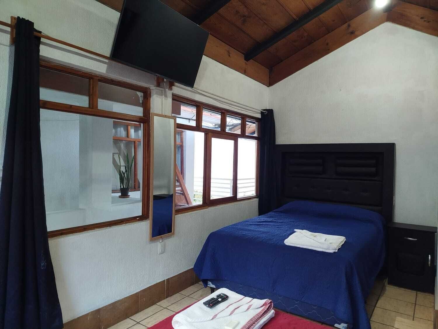 A bedroom with a bed, a TV mounted on the wall, and a window with curtains.