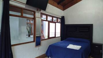 A bedroom with a bed, a TV mounted on the wall, and a window with curtains.
