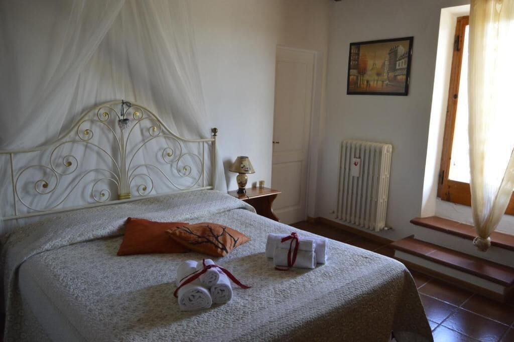 Una cama con dosel, una mesita de noche con lámpara, un radiador y un cuadro en la pared.