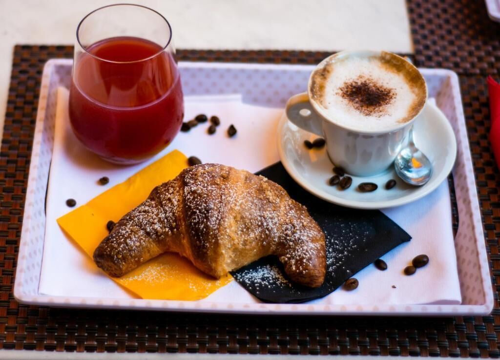 Una bandeja con un croissant, una taza de café y un vaso de bebida roja.