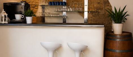 A bar area with two white bar stools, a coffee machine, a clock, and a stone wall.