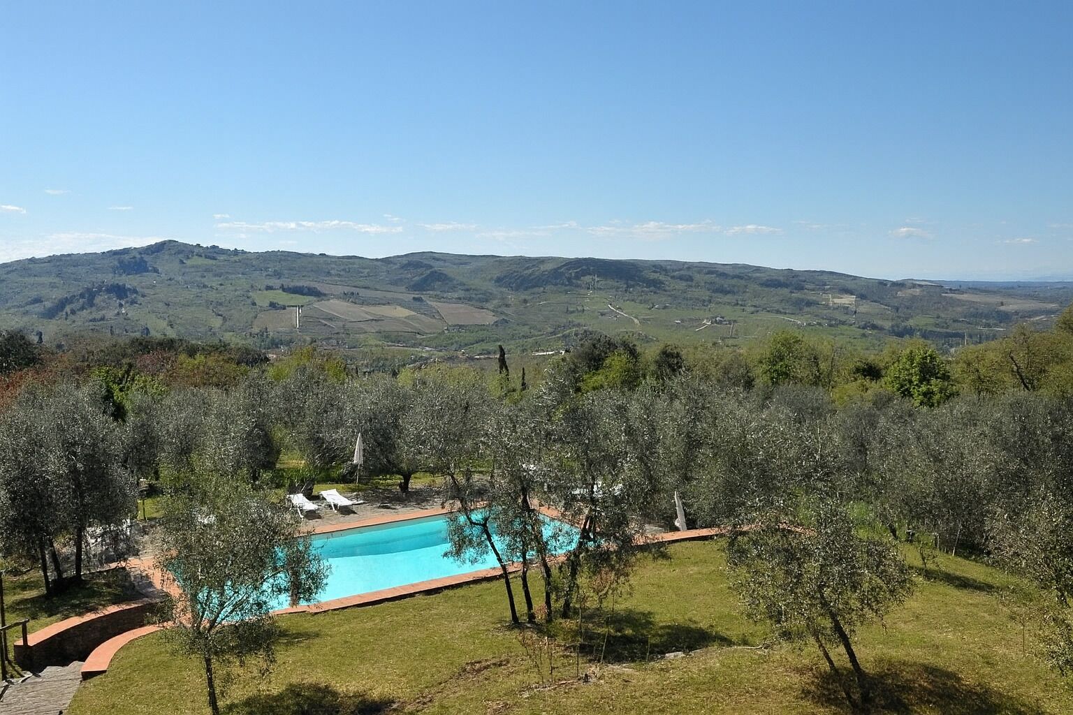 Una piscina rodeada de árboles, con vistas a colinas distantes.